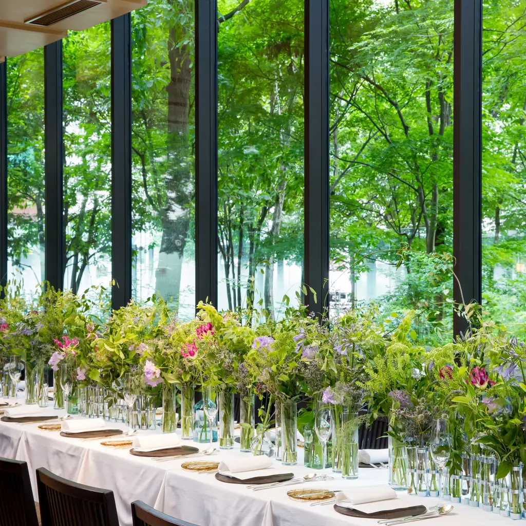 A long table laid for a celebration at the Café, with flowers and the window onto the forest’s green.