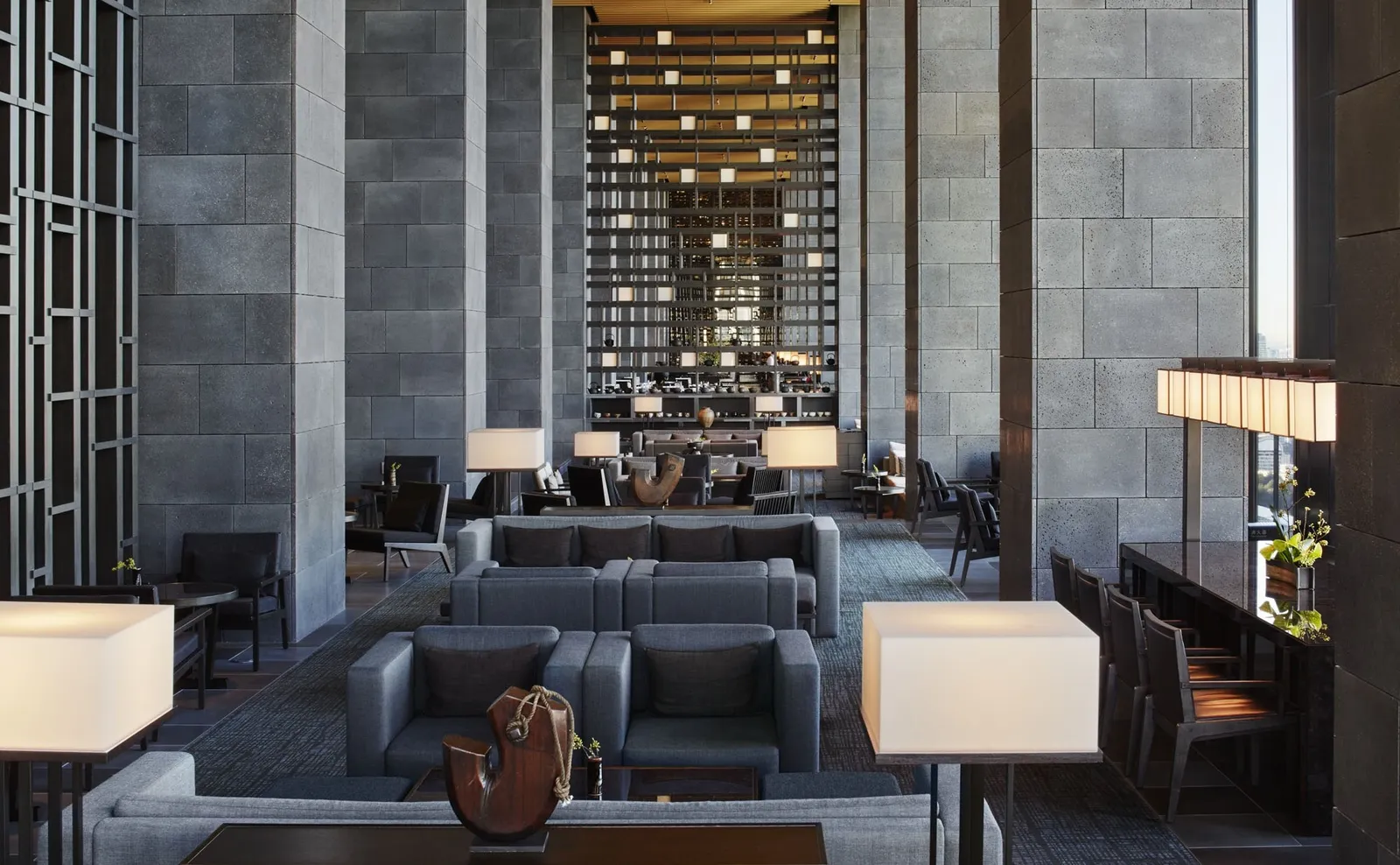 The Lounge on the 30-third floor: grey sofas between stone walls and a wall of lights rising to the ceiling.