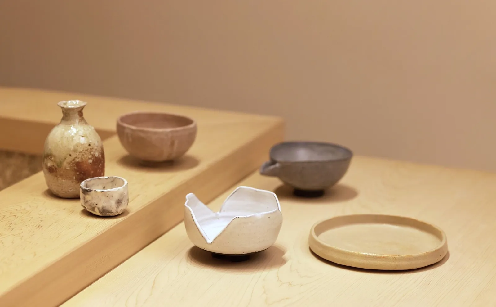 Musashi by Aman’s handmade pottery, a sake flask and bowls, on the pale wood counter.