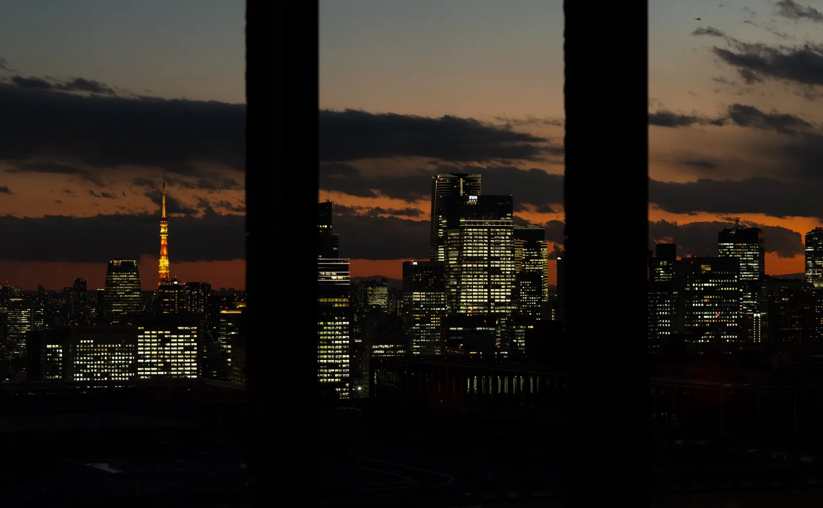 Tokyo at nightfall between 2 pillars: Tokyo Tower lit up and the towers below the sunset clouds.