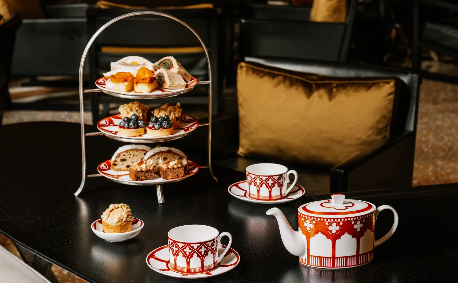 Afternoon tea on a black table: the 3-tier stand of pastries and sandwiches, the teapot and decorated cups.