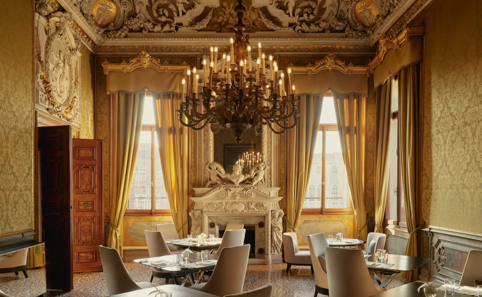 Arva’s dining room: gold silk walls, the marble fireplace, the chandelier and tables laid between the windows onto the canal.