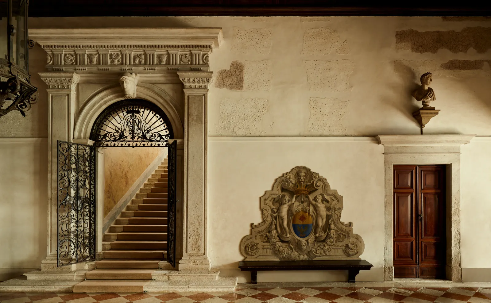 The palazzo’s entrance: the stone portal with its gate, the carved coat of arms and the staircase rising beyond.