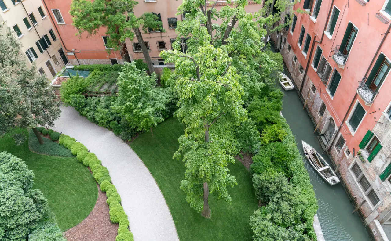 The entrance garden from above: the pale path between the lawn and the trees, beside a canal with a boat.