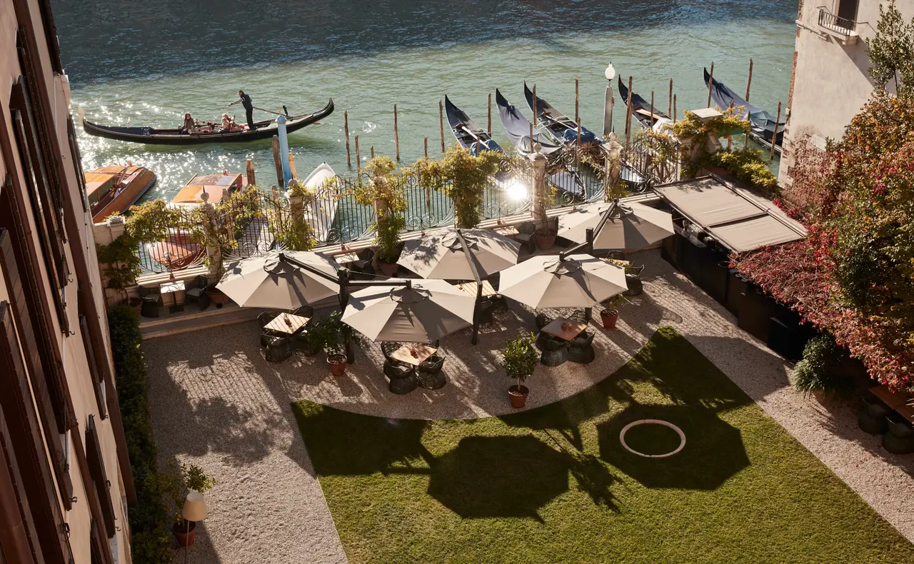 The garden on the Grand Canal from above: the lawn, parasols over the tables and, beyond the railing, gondolas on the water.