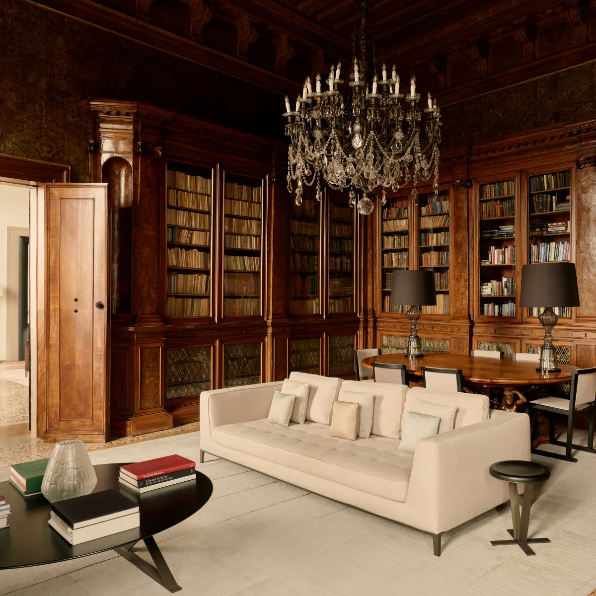 The library: dark timber bookcases up to the ceiling, a crystal chandelier and a white sofa.