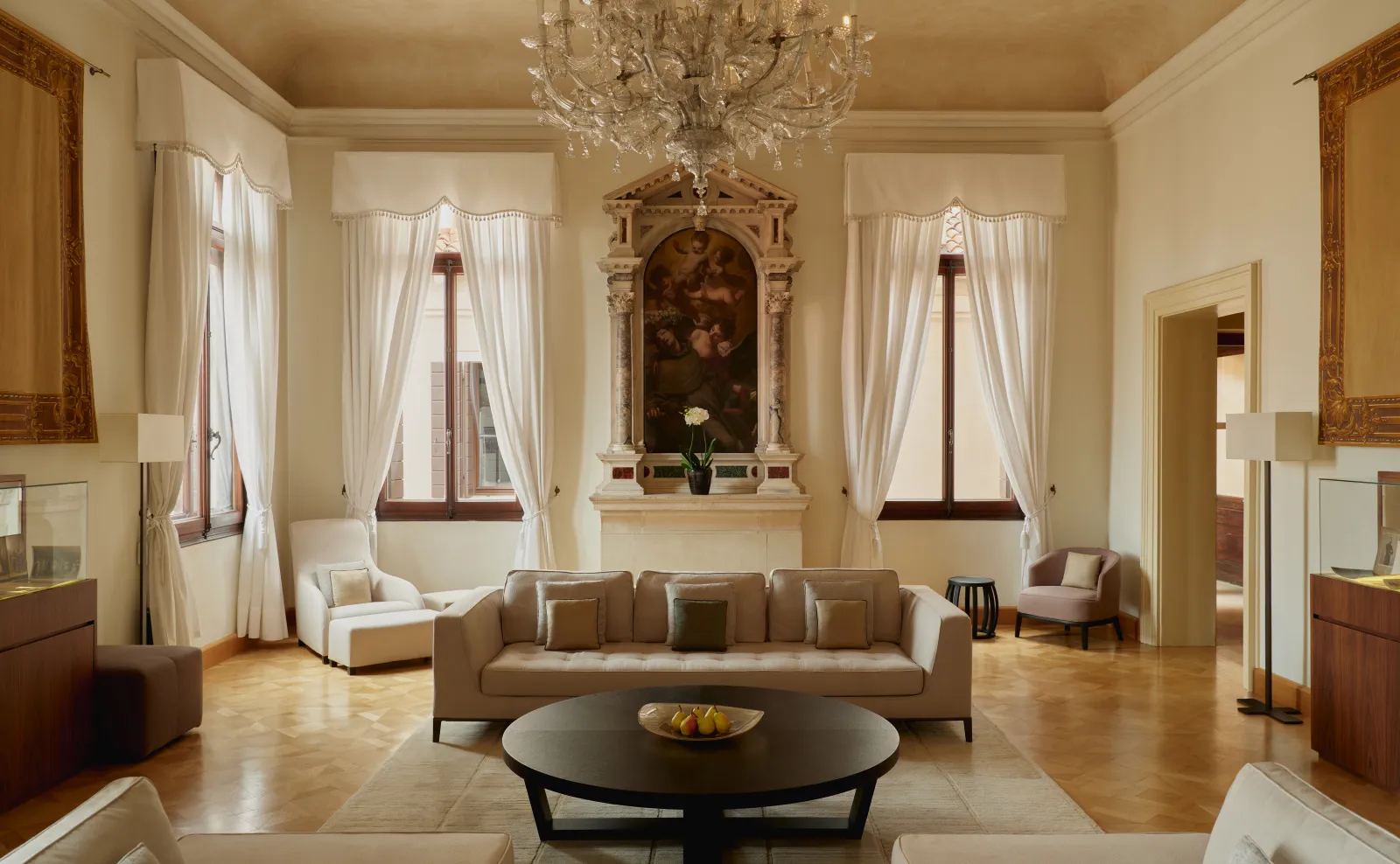 The Coccina’s Apartment living room: a crystal chandelier, a painting above the fireplace, the sofas and the tall windows.