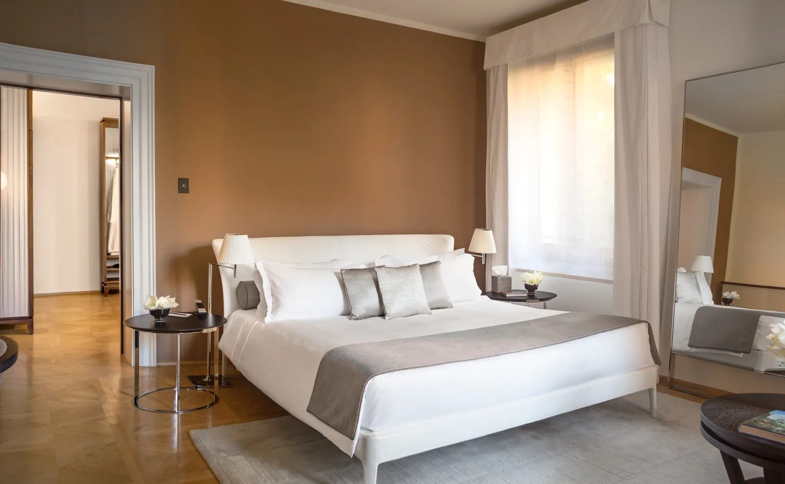 A Palazzo Bedroom: the king bed, ochre walls, parquet floor and white curtains on the window over the garden.