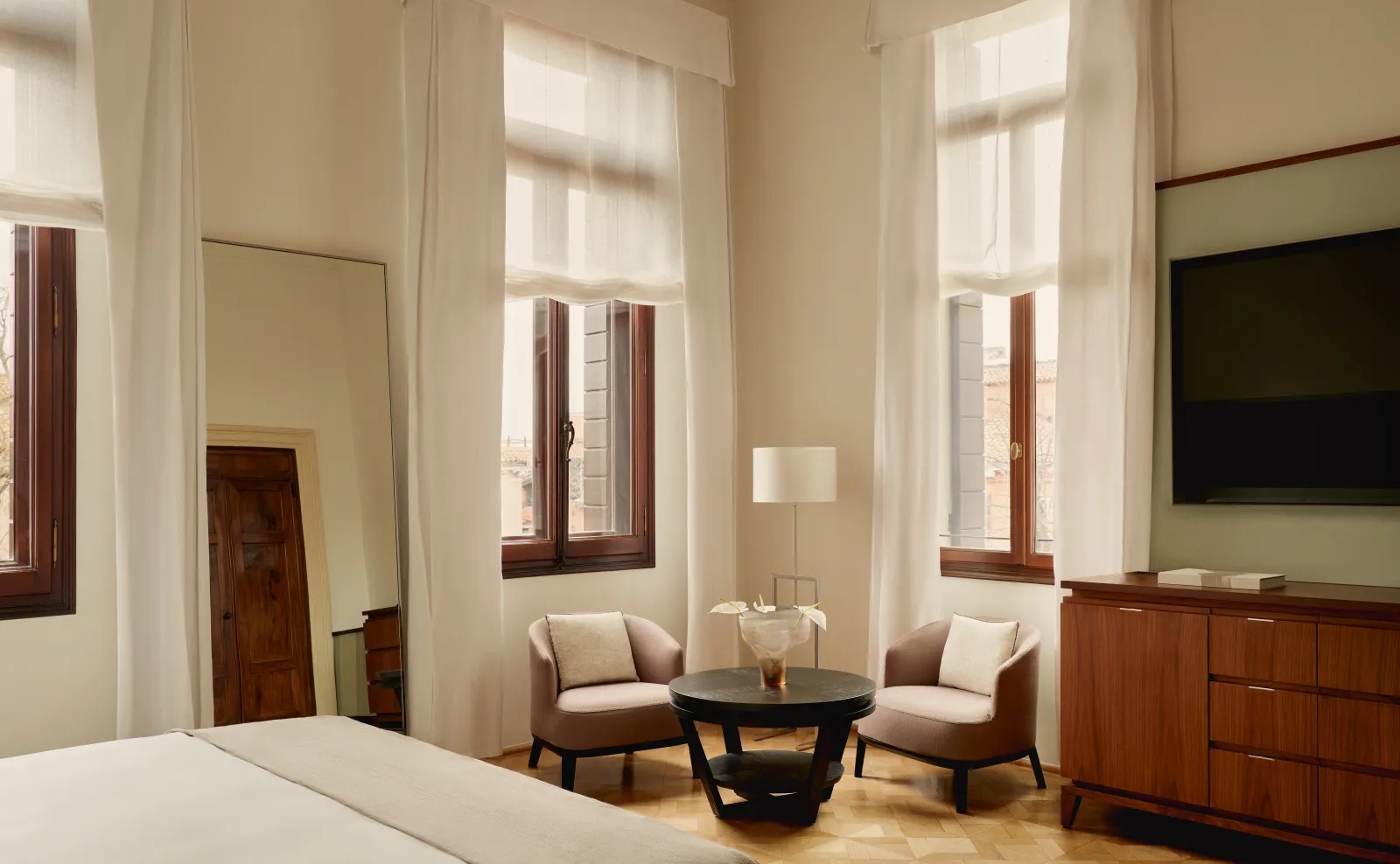 A Palazzo Chamber Affresco: the bed, 2 armchairs by the tall windows and an old timber door.