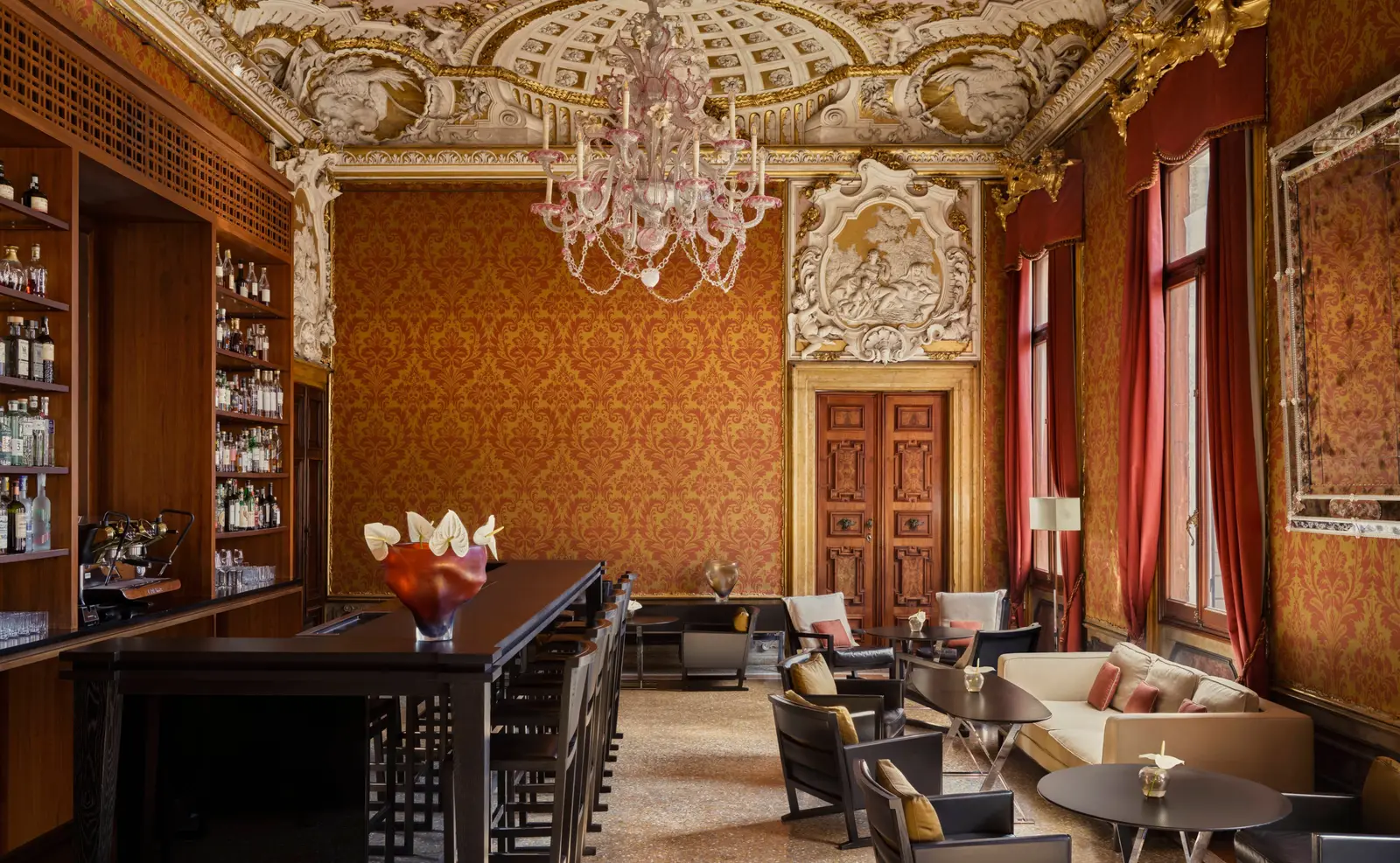 The Bar in the Red Room: the frescoed ceiling, the glass chandelier, the dark counter and sofas between red damask walls.