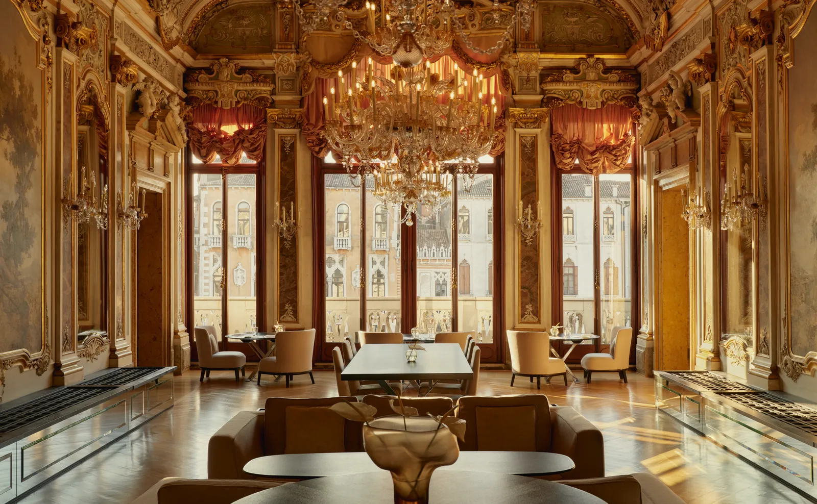 A room on the piano nobile with gilded stucco, mirrors, a great crystal chandelier and the windows open onto the Grand Canal.