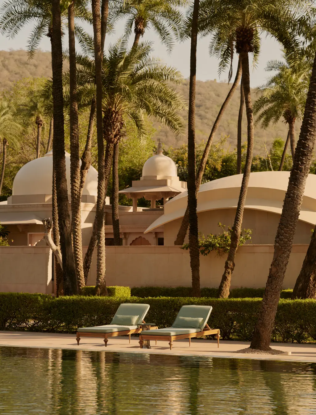 The pool among palms, 2 loungers at its edge and the pavilions’ domes behind