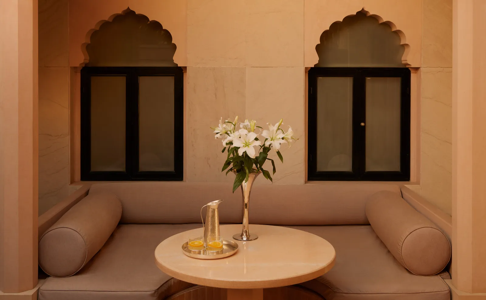 A Courtyard Haveli Suite’s courtyard, with cushioned seats beneath 2 arched niches and a round table