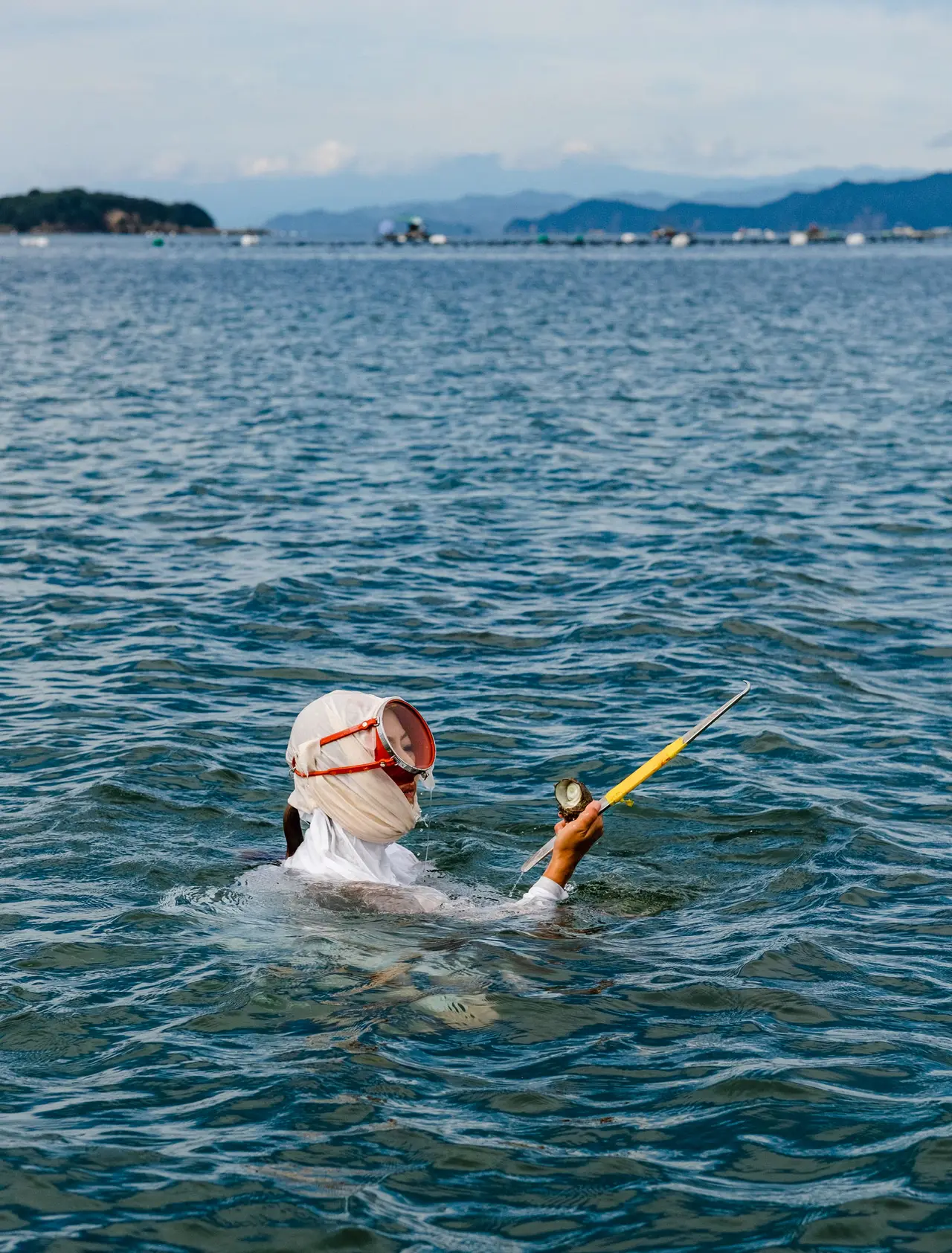 An ama diver in a white head cloth and mask, surfacing in the bay with her catch