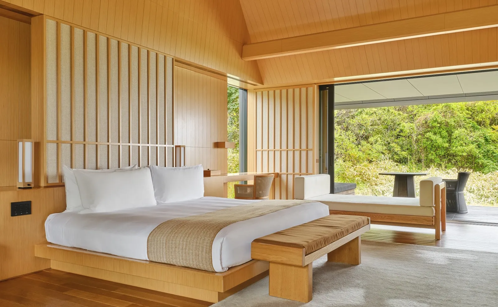A platform bed in pale timber, the veranda and the garden beyond