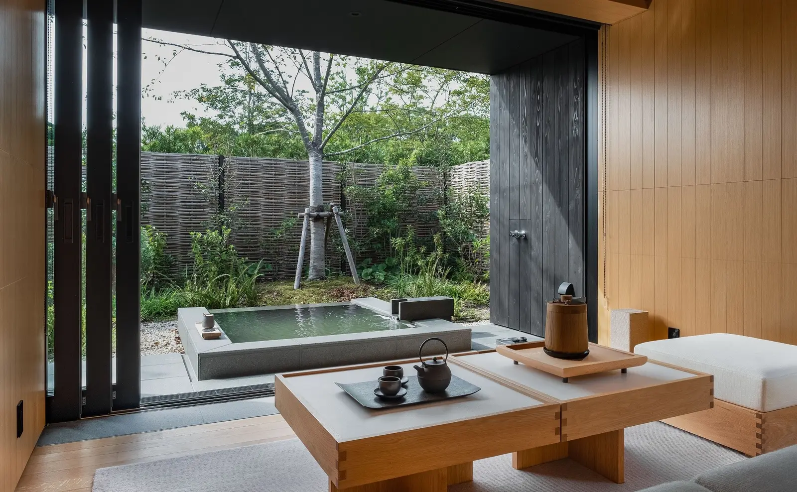 A low table and a tea set facing the garden onsen behind a woven fence