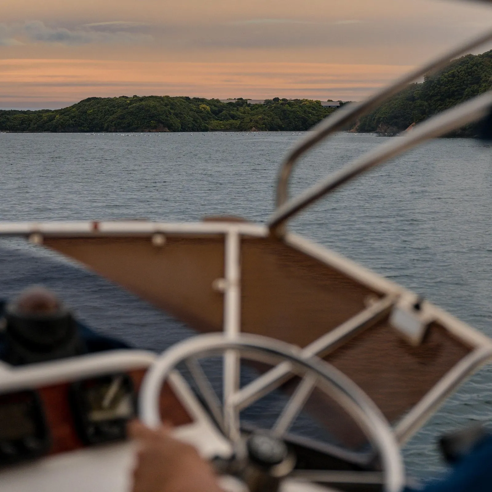 The helm of a boat on Ago Bay at sunset, a wooded island ahead