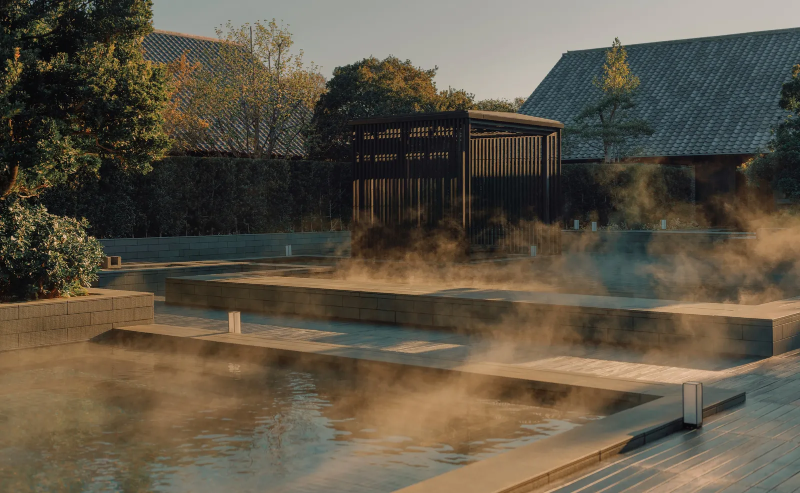 Steam rising off the spa’s open-air thermal pools at dawn, a dark timber pavilion behind