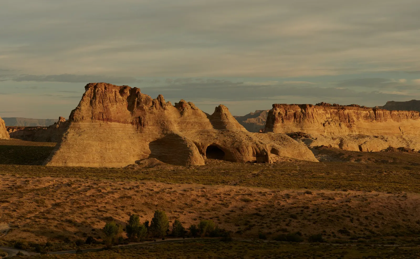 The sandstone formations around Broken Arrow Cave in golden light, the dark arch of the cave and the scrub plain.