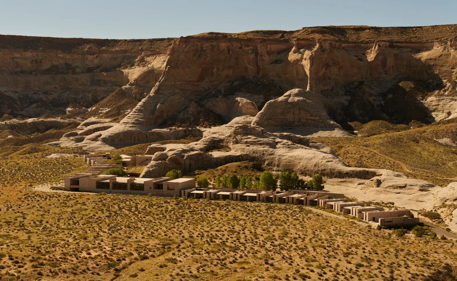 The resort from above: a low line of sand-coloured concrete suites at the foot of a great mesa, on the desert plain.