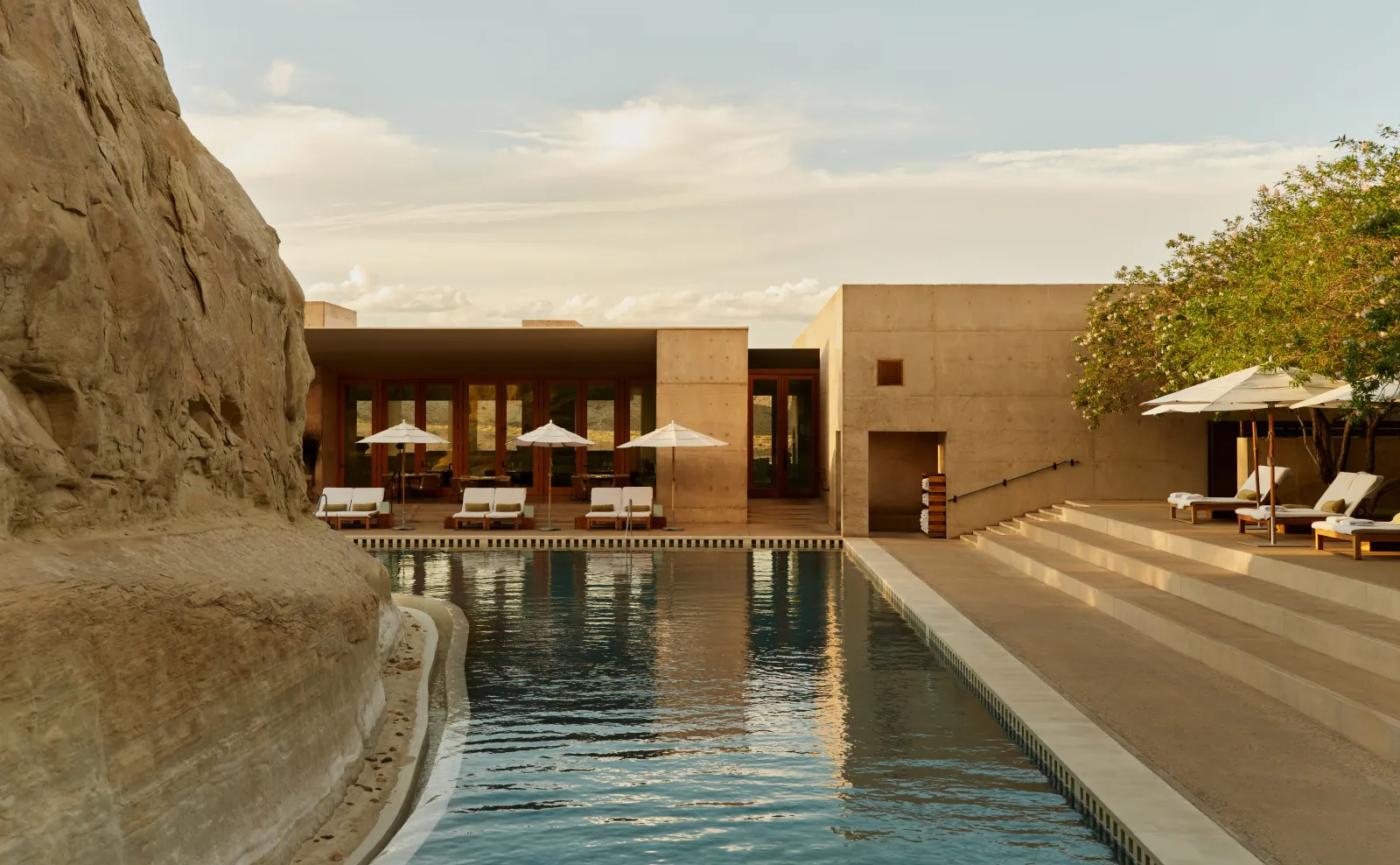 The main pool by day, its green water lapping the rock on the left, daybeds and parasols before the pavilion.