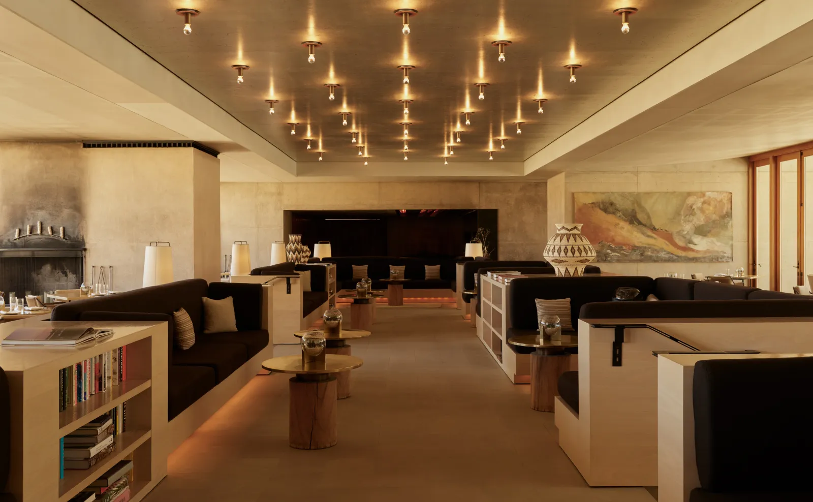 The library: a long room with dark sofas, bookshelves, a fireplace and rows of small ceiling lights.