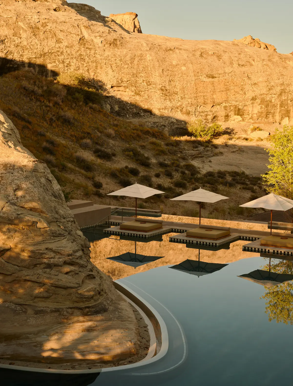 The pool in early light: still water reflecting the parasols and the rock wall that closes it on the left.