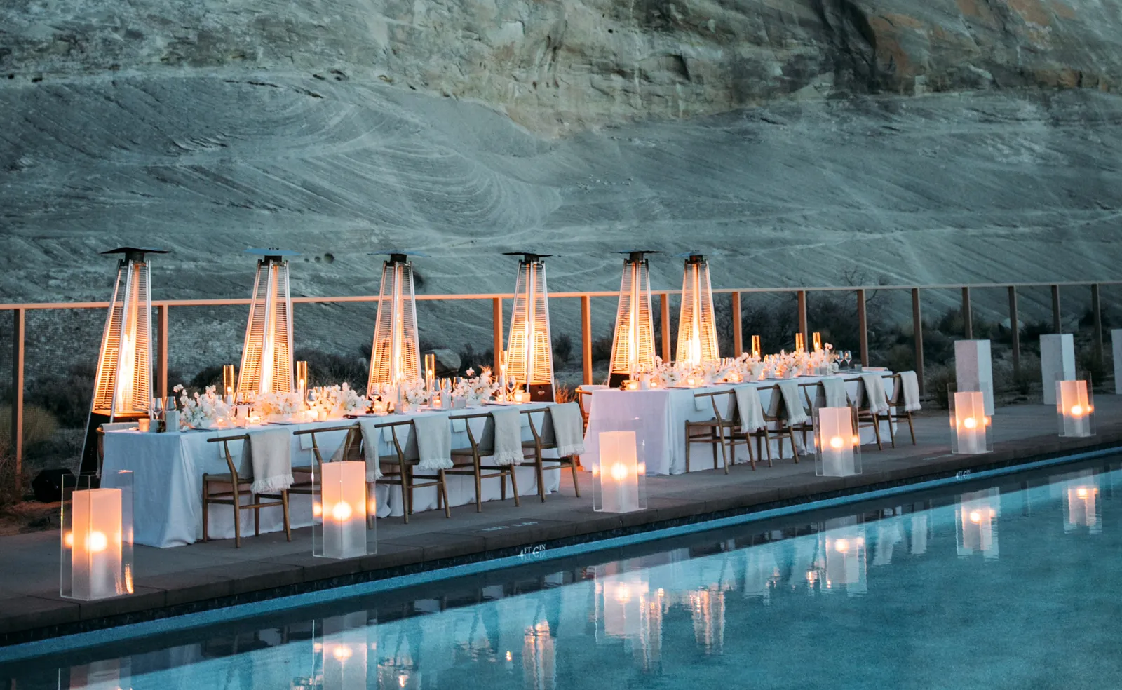 A long candlelit table beside the pool, patio heaters burning under the rock wall.