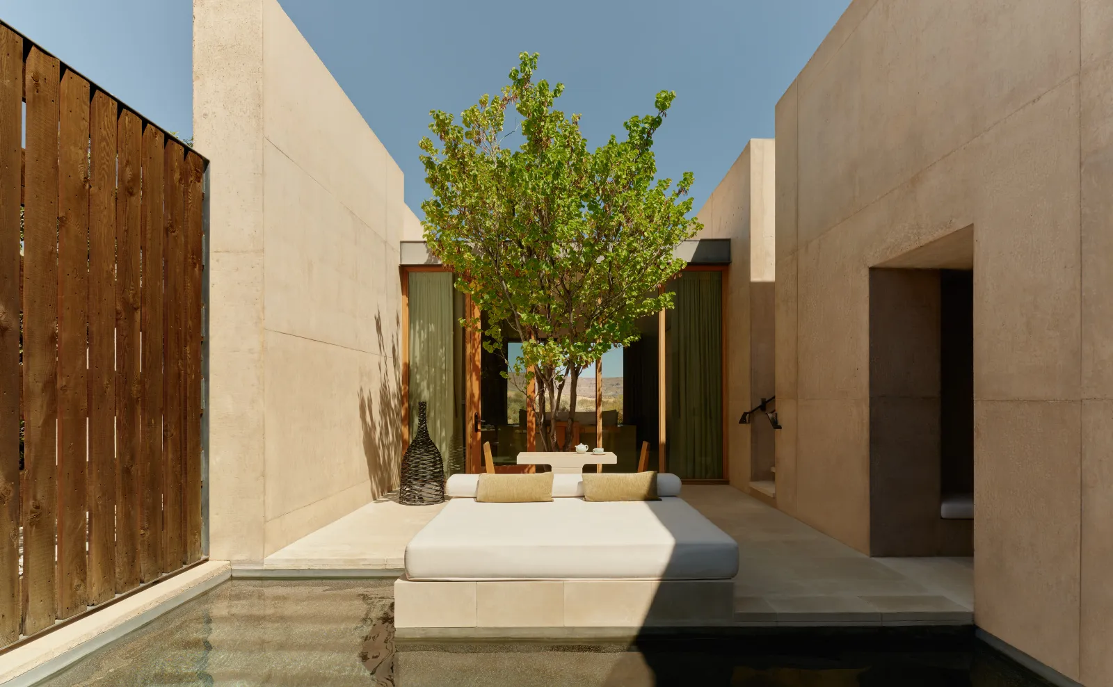 A Desert Pool Suite’s courtyard: a daybed over the water, a tree and concrete walls open to the desert.
