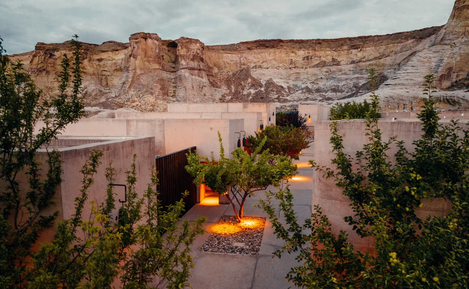 The lanes between the suites at dusk, with fruit trees, ground lights and the cliff above the flat roofs.