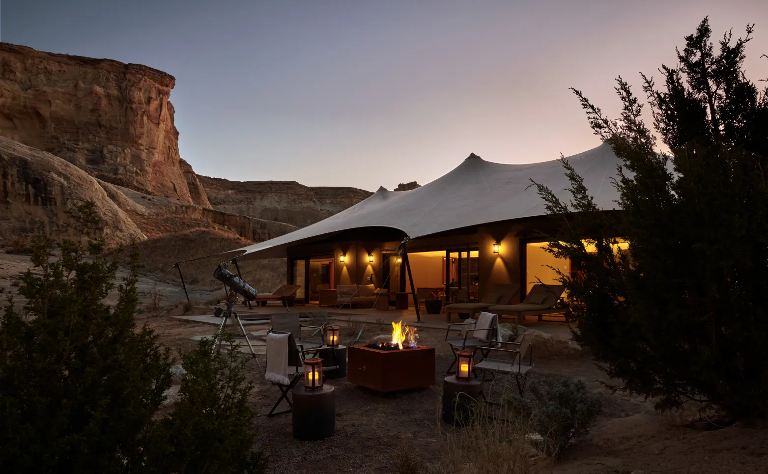 The Grand View pavilion at dusk: the lit tent, a burning fire pit, a telescope and the cliffs behind.