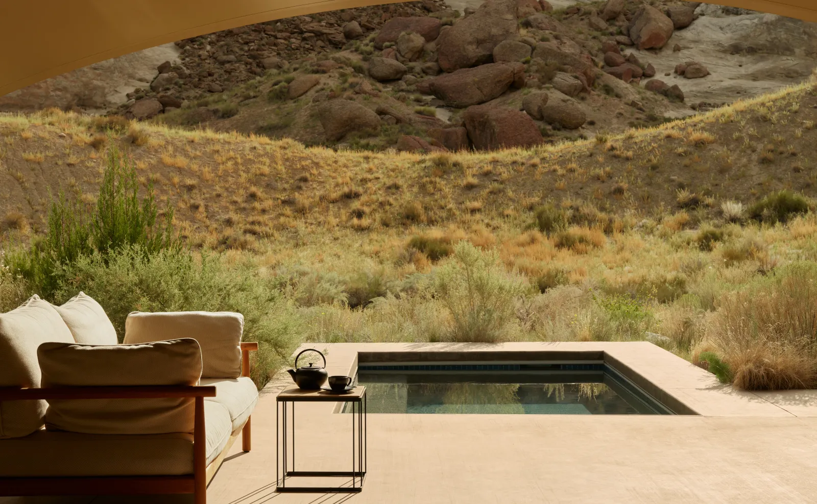 A one-bedroom pavilion’s terrace: a sofa, a small table with a teapot and the pool before a slope of boulders.