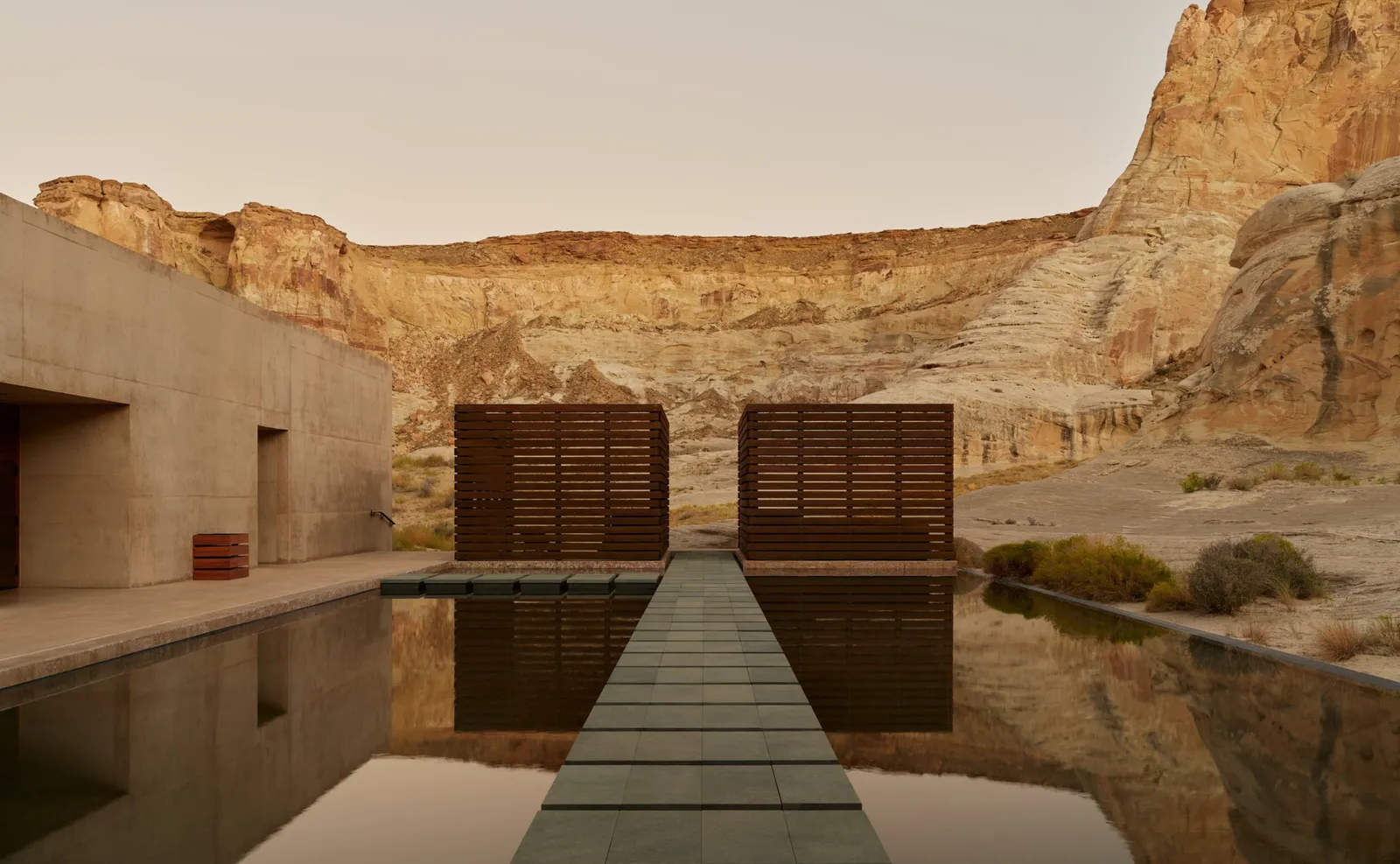 The spa’s reflection pool: a stone walkway over the water leads to 2 slatted wooden doors, under the cliff.