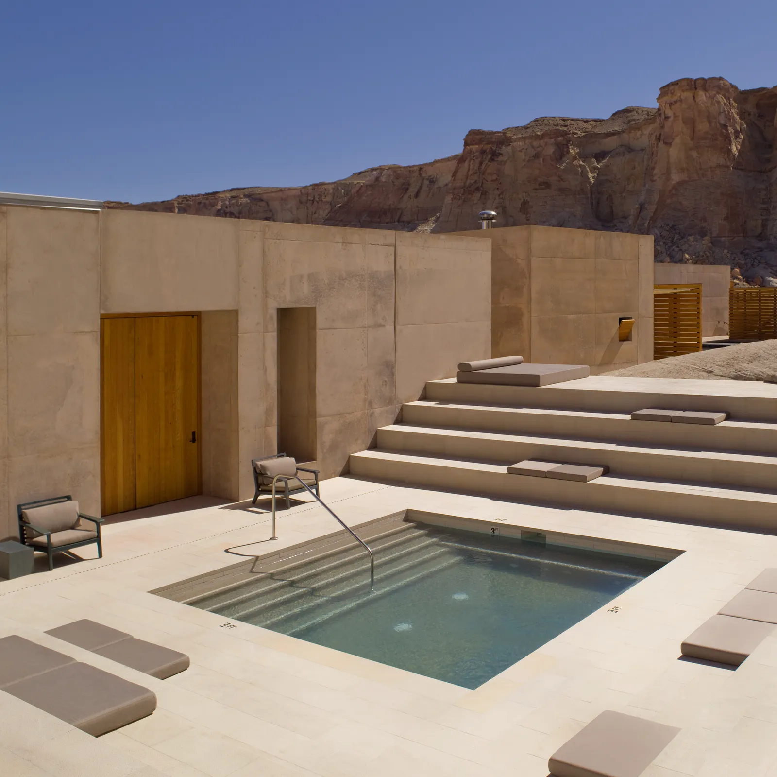 The spa’s step pool in a pale stone court, with a wooden door and the cliff beyond the wall.
