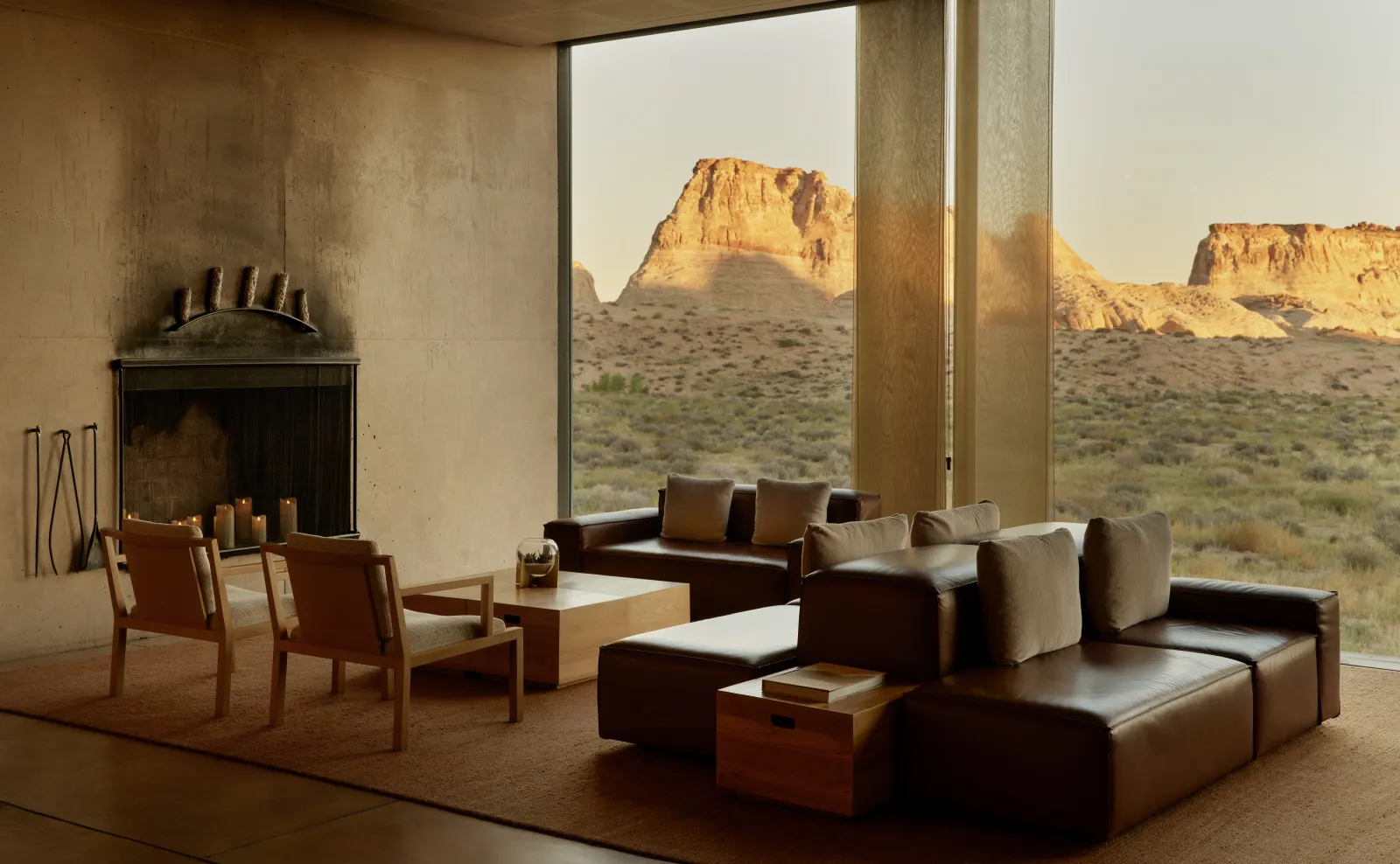 The central pavilion’s living room: dark leather sofas, wooden armchairs and a fireplace before the window onto the mesas at sunset.