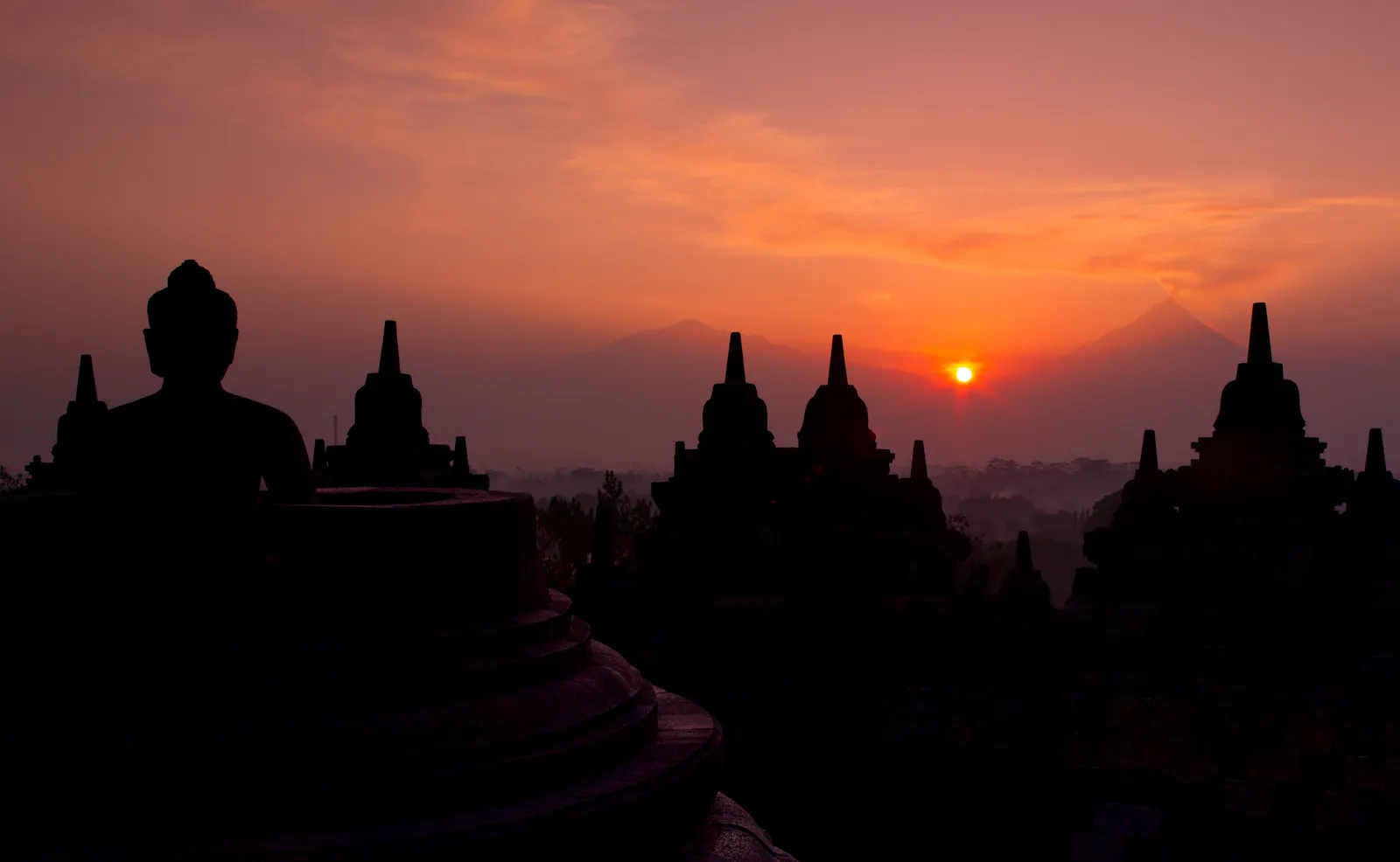 Borobudur’s stupas and a seated Buddha in silhouette against the rising sun