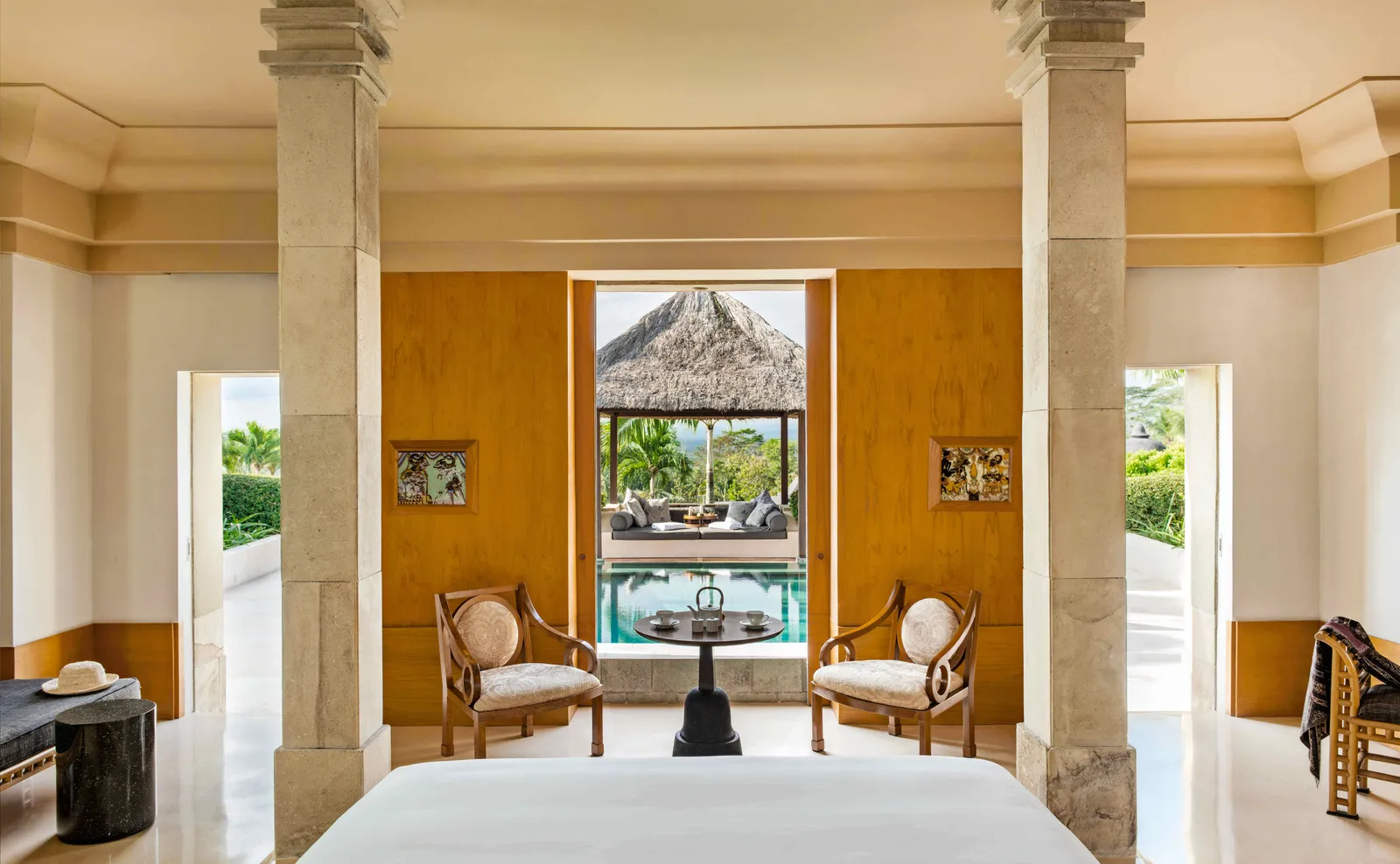 A pavilion bedroom between stone columns, looking through to its pool and balé
