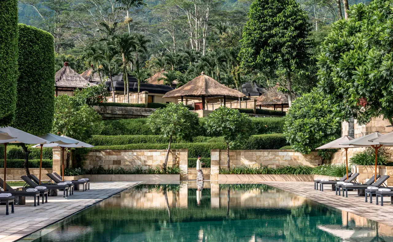 The long green-stone pool with loungers, pavilions on the slope above