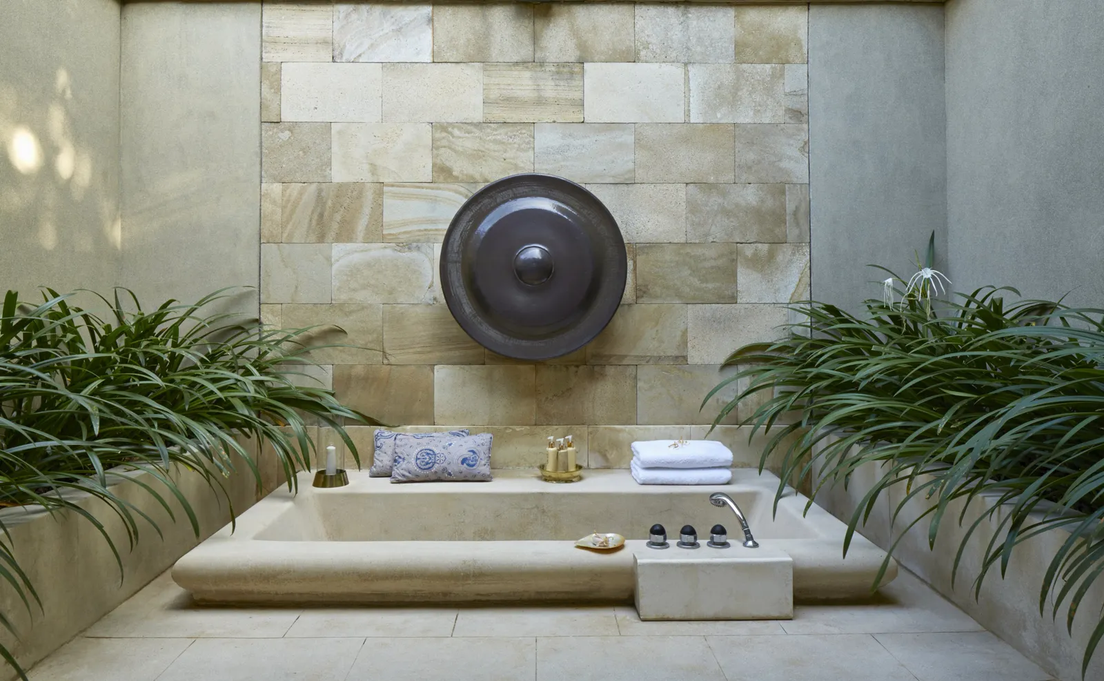 A sunken stone bath open to the sky, a bronze gong on the wall behind