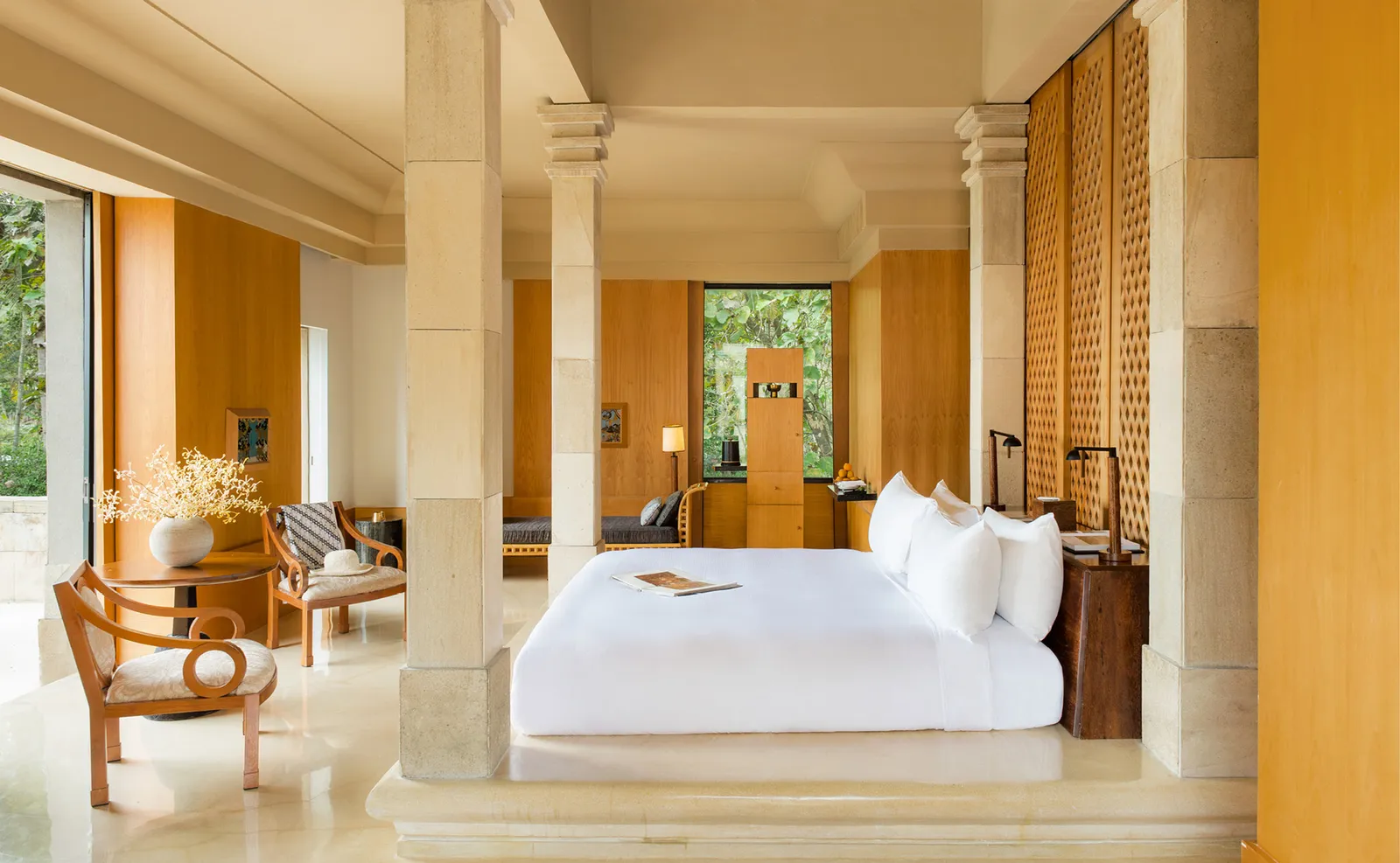 A white bed on its platform between stone columns and timber screens