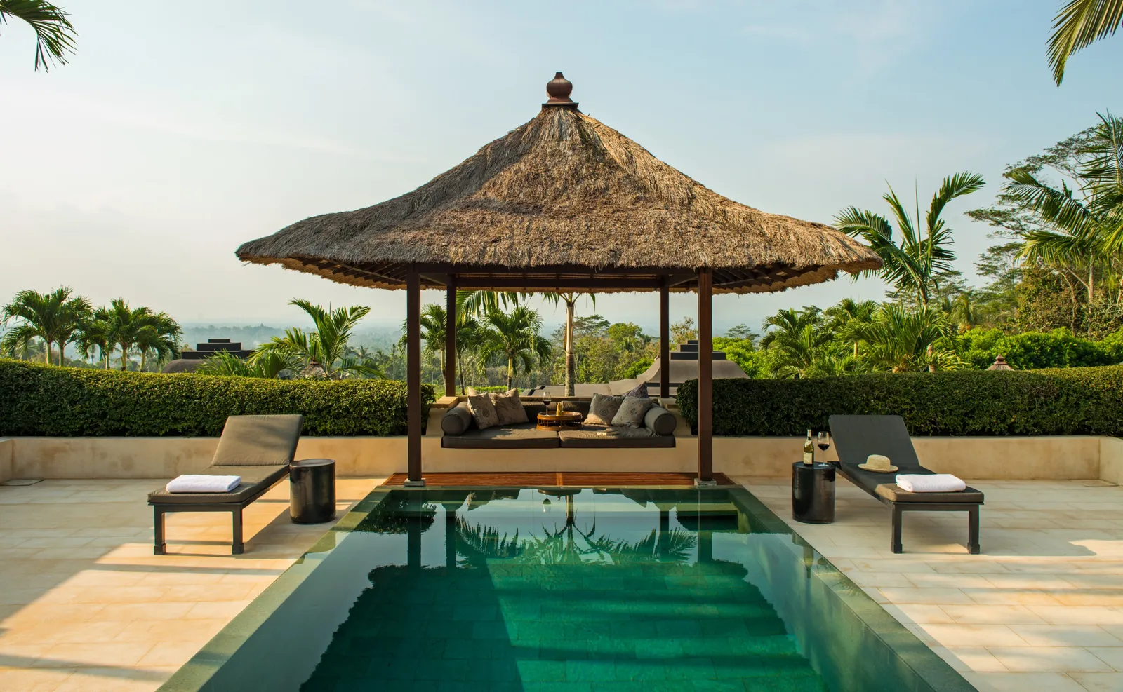A pool and a thatched balé on a terrace, the valley beyond the hedge