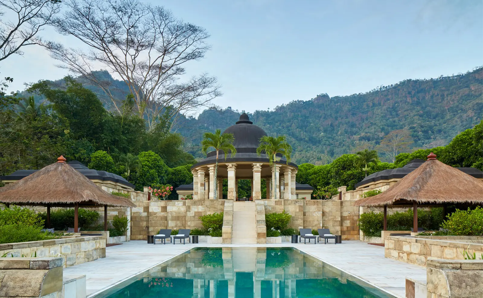 A long pool leading to a domed rotunda, forested hills behind
