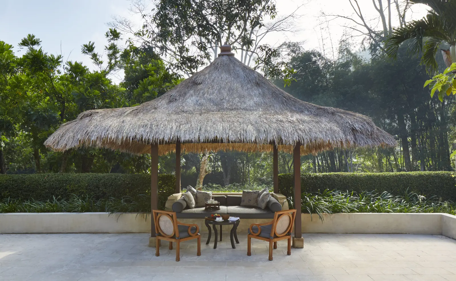 A thatched balé with chairs and a daybed in a walled garden