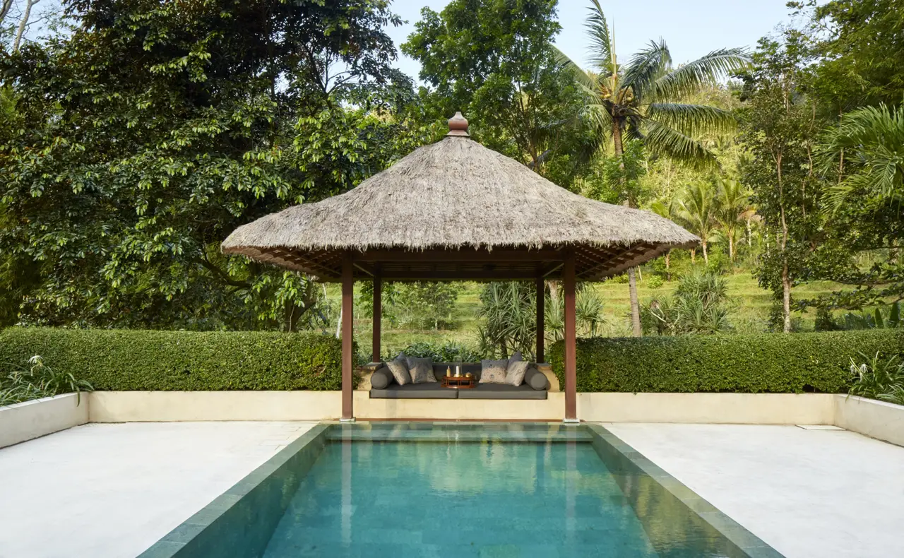 A pool in front of a thatched balé, trees and hills behind