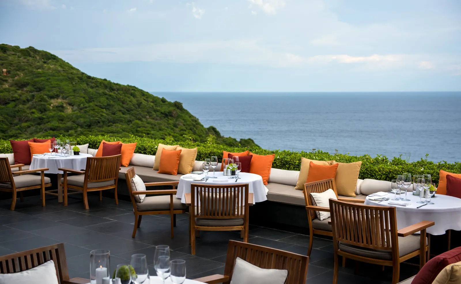 The Restaurant terrace with orange cushions, laid tables and the sea beyond the hedge
