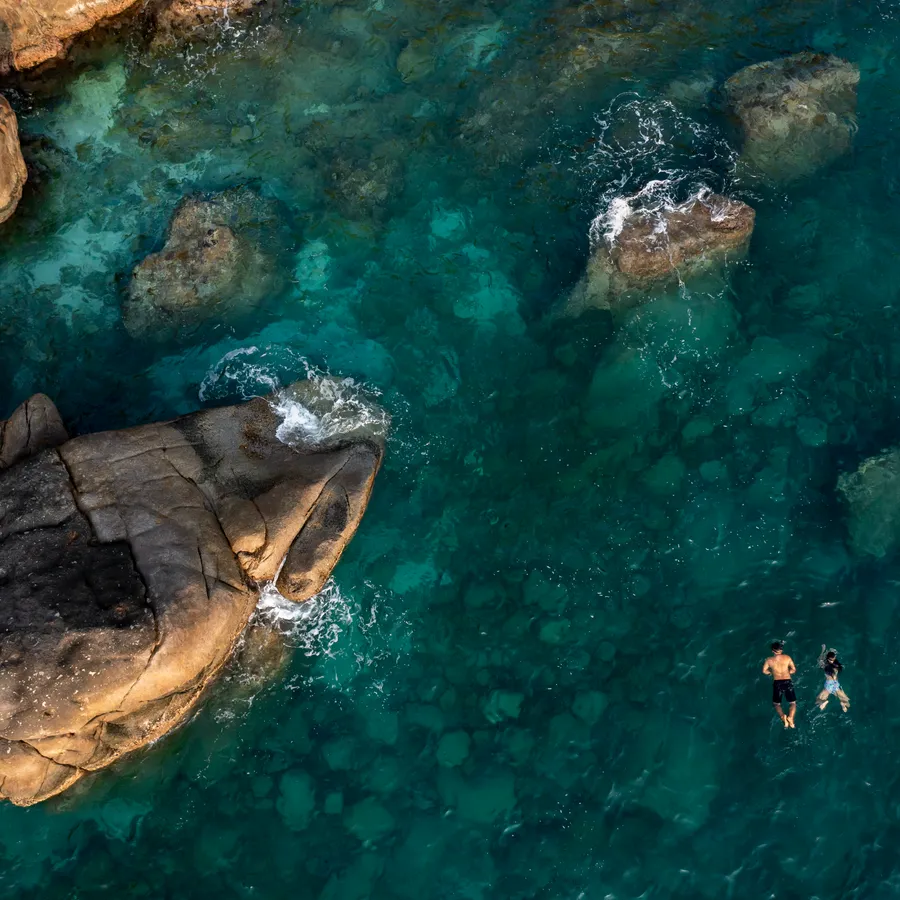 2 snorkellers over the seabed between the rocks, seen from above