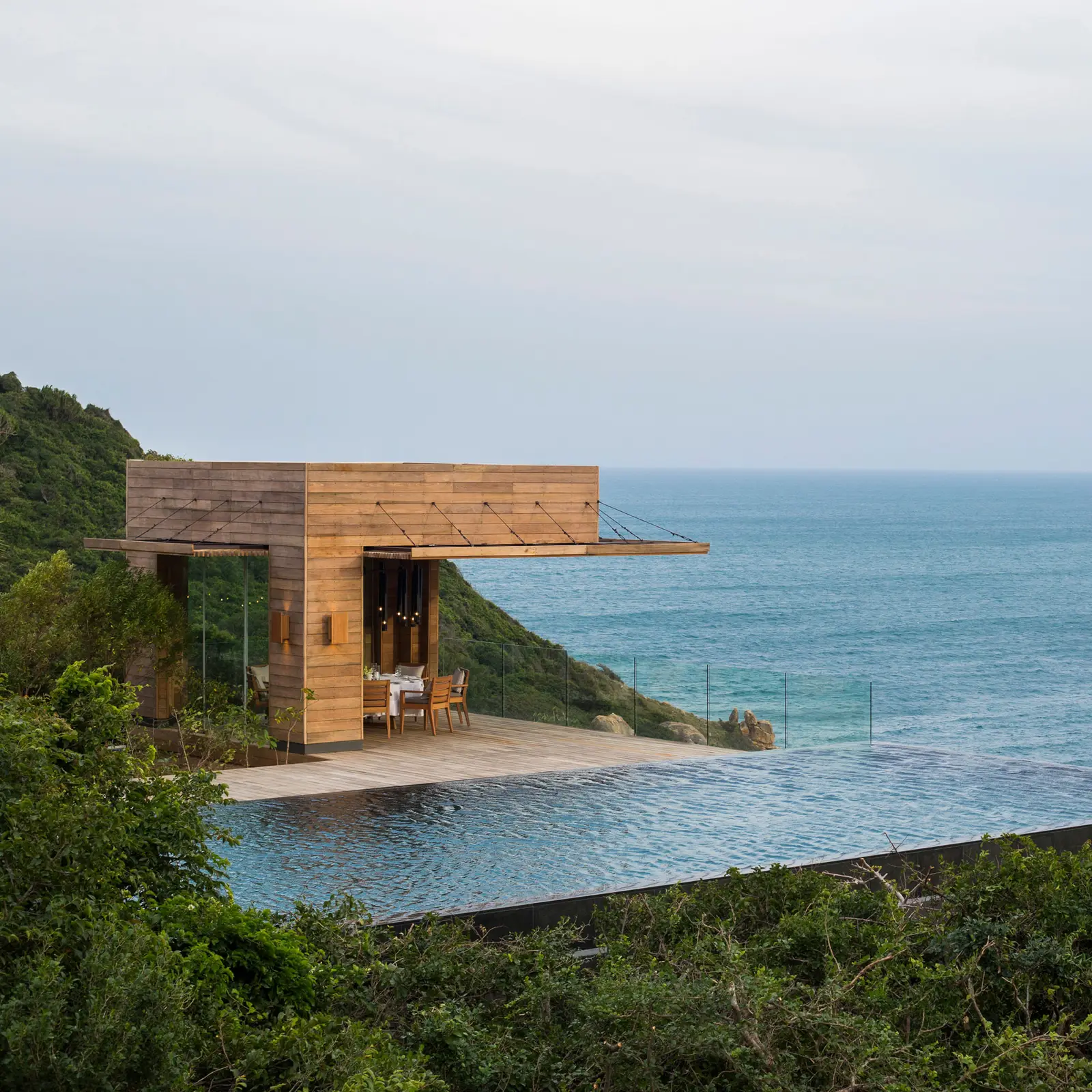 A timber pavilion above an infinity pool at the edge of the cliff, facing the open sea