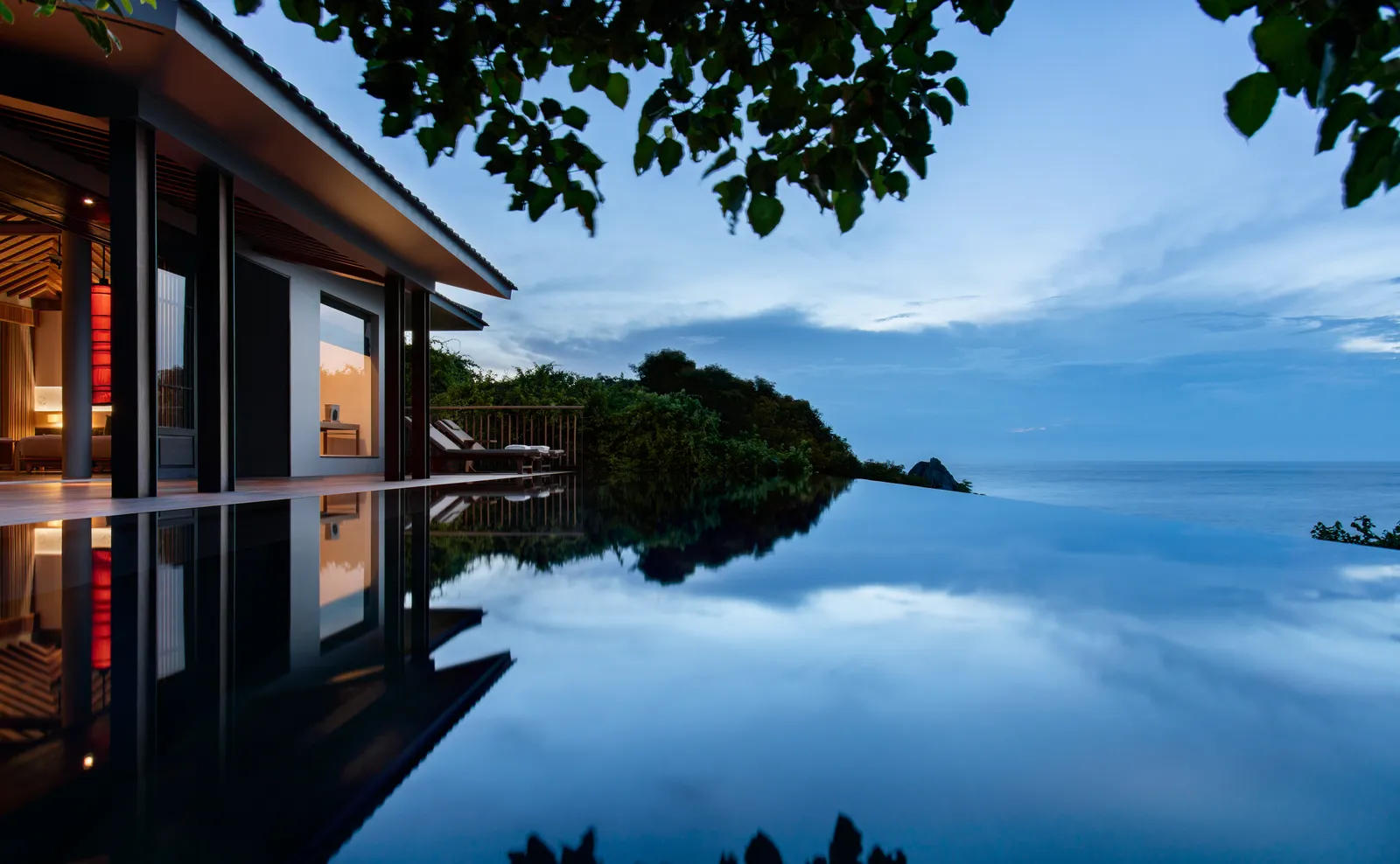 An Ocean Pool Villa’s infinity pool at dusk, with the sea and an island behind