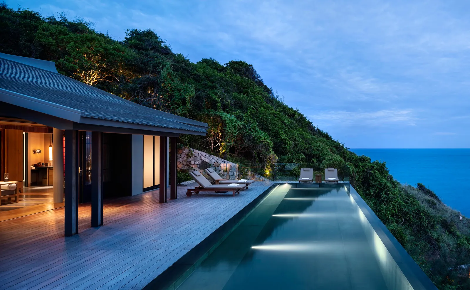 The One-Bedroom Ocean Pool Residence at dusk: the long pool and loungers above the sea
