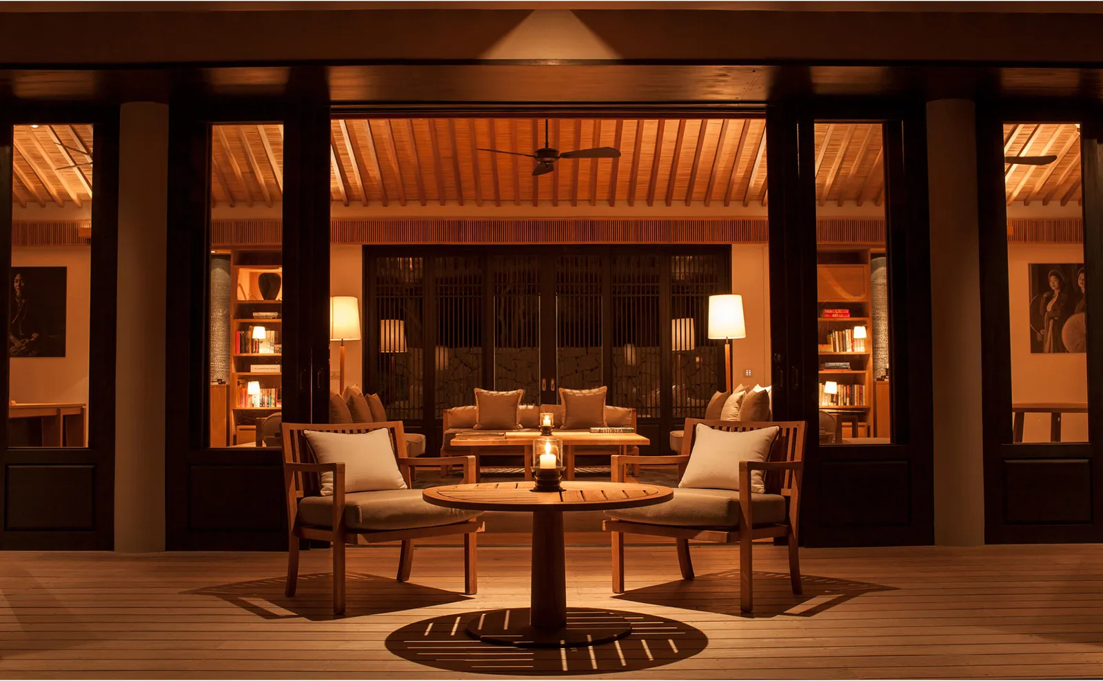 The living pavilion of the Three-Bedroom Pool Residence lit at night, with armchairs and a table